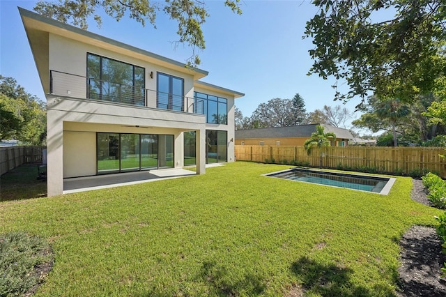 rear view of property featuring a patio area, a balcony, a fenced in pool, and a yard