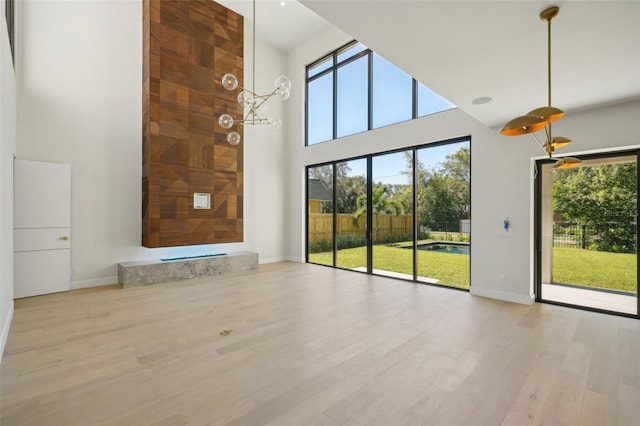 unfurnished living room featuring a notable chandelier, light wood-type flooring, and a towering ceiling