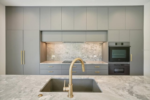 kitchen with tasteful backsplash, light stone counters, gray cabinetry, and sink