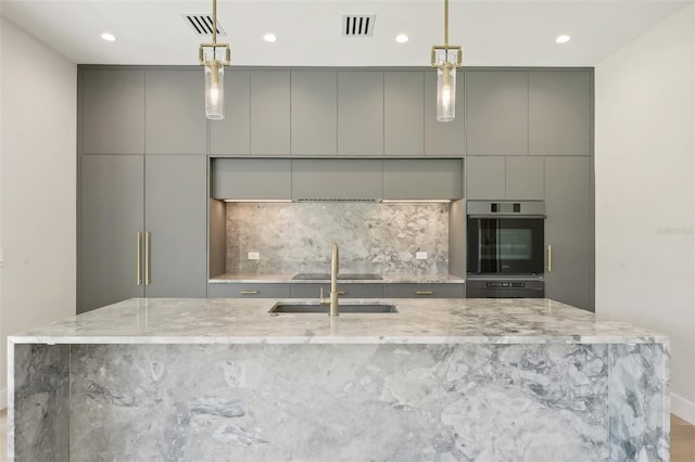 kitchen with gray cabinets, a spacious island, light stone countertops, and sink