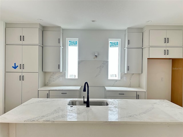 kitchen with a center island with sink, light stone countertops, sink, and tasteful backsplash