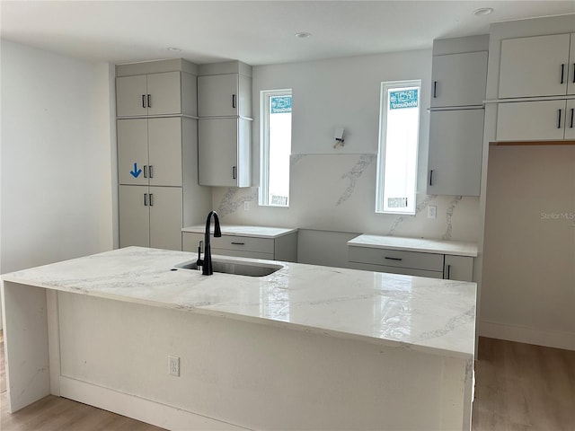 kitchen with light stone counters, sink, wood-type flooring, plenty of natural light, and an island with sink