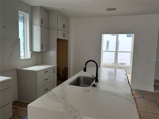 kitchen featuring light stone countertops, sink, and a kitchen island with sink