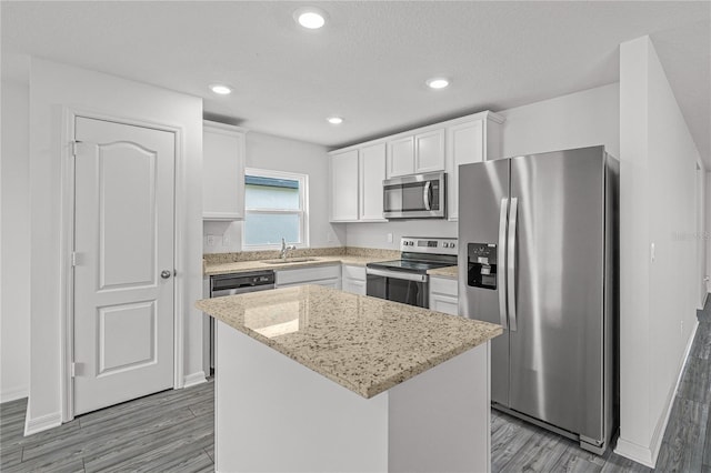 kitchen with appliances with stainless steel finishes, sink, light wood-type flooring, a kitchen island, and white cabinetry