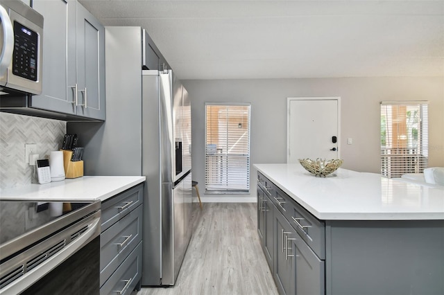 kitchen featuring light hardwood / wood-style floors, backsplash, stainless steel appliances, and gray cabinets