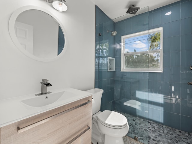 bathroom featuring toilet, vanity, and a tile shower