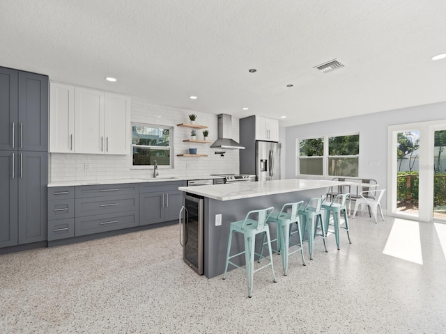 kitchen with stainless steel fridge with ice dispenser, a kitchen bar, backsplash, wall chimney range hood, and sink