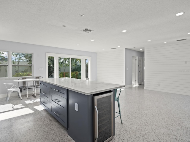 kitchen with light stone counters, a center island, plenty of natural light, and beverage cooler