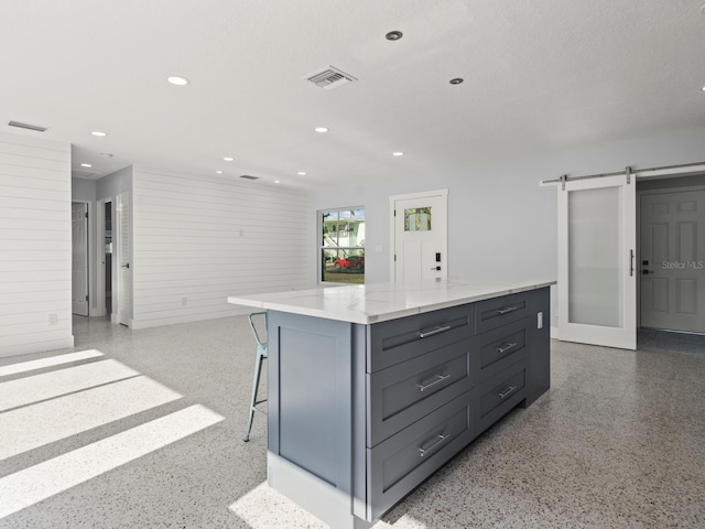 kitchen featuring a kitchen island, a barn door, gray cabinets, a breakfast bar area, and light stone countertops