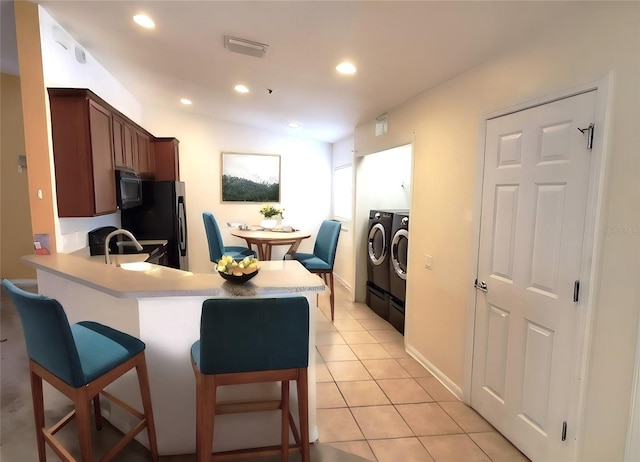 kitchen with light tile patterned floors, a kitchen breakfast bar, black fridge, separate washer and dryer, and kitchen peninsula