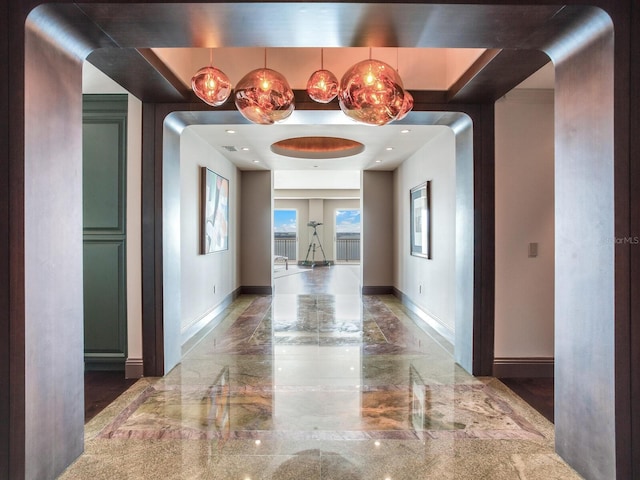 hallway featuring marble finish floor, a raised ceiling, and baseboards