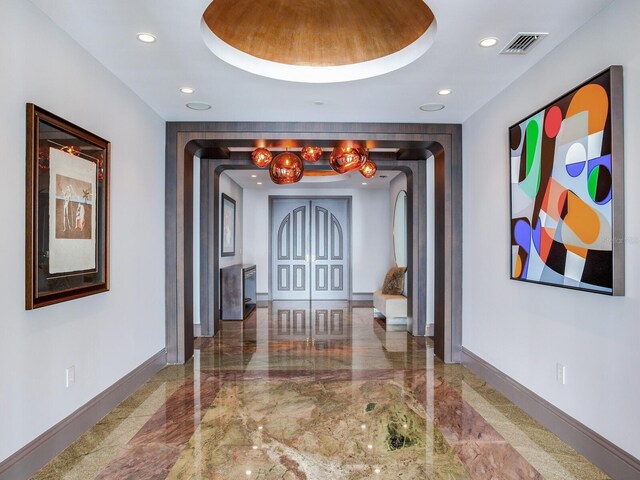 hall featuring marble finish floor, a tray ceiling, visible vents, and baseboards