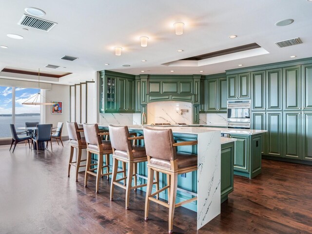 kitchen with a raised ceiling, green cabinetry, a center island with sink, and visible vents