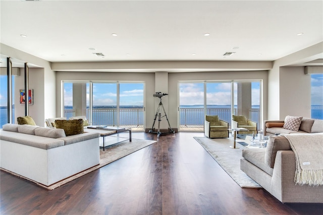 living room featuring dark wood-style flooring, visible vents, and a water view