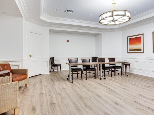 dining area featuring a raised ceiling, visible vents, a decorative wall, light wood-style flooring, and ornamental molding