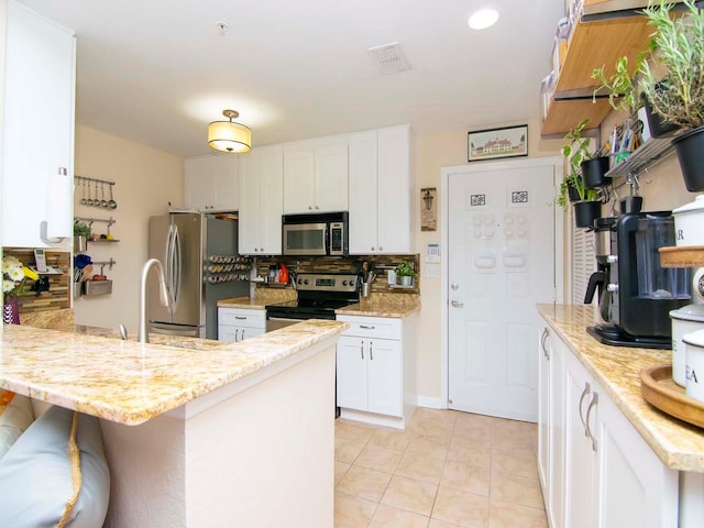 kitchen with white cabinets, stainless steel appliances, light tile flooring, light stone countertops, and tasteful backsplash