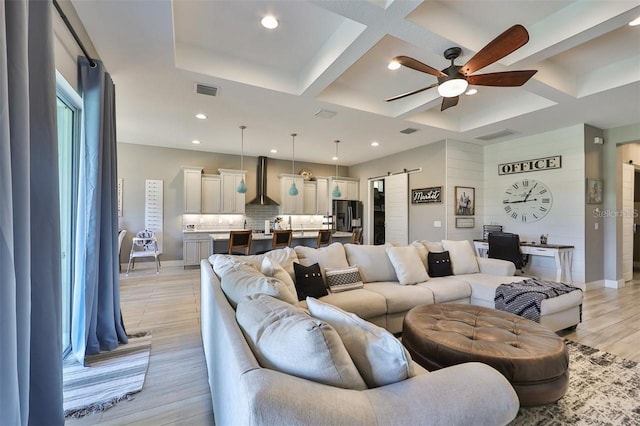 living room with light wood-type flooring, ceiling fan, coffered ceiling, a barn door, and beam ceiling