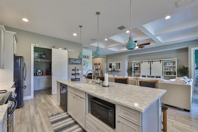 kitchen featuring an island with sink, sink, white cabinetry, black appliances, and a barn door