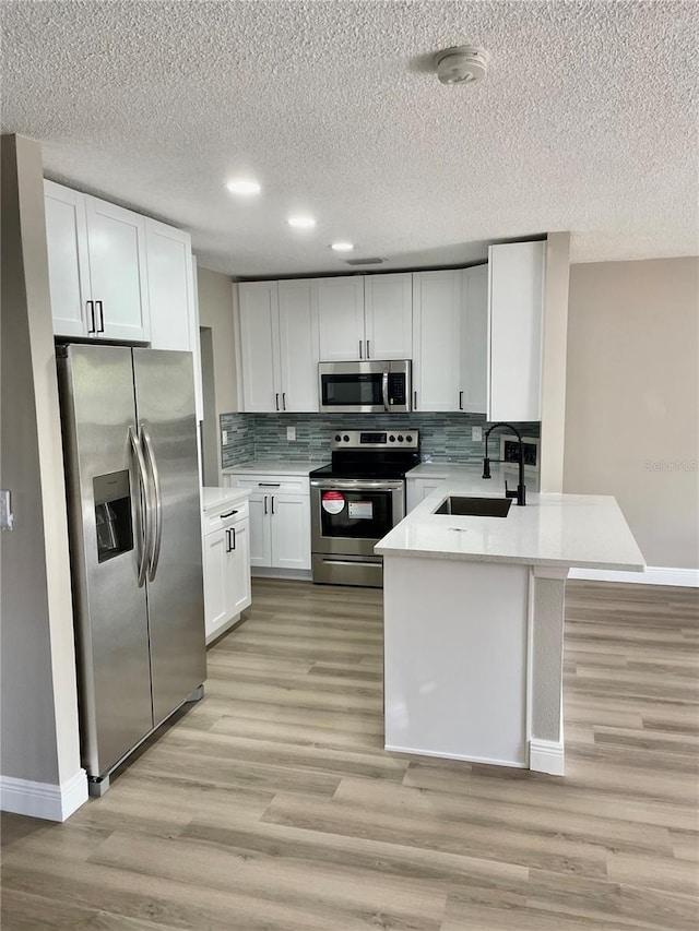 kitchen featuring sink, light wood-type flooring, stainless steel appliances, white cabinets, and tasteful backsplash