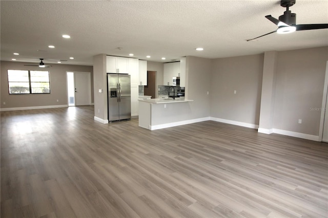 unfurnished living room featuring a textured ceiling, ceiling fan, sink, and light wood-type flooring