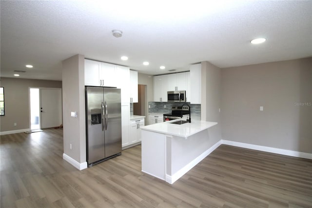 kitchen featuring stainless steel appliances, hardwood / wood-style flooring, kitchen peninsula, white cabinets, and backsplash