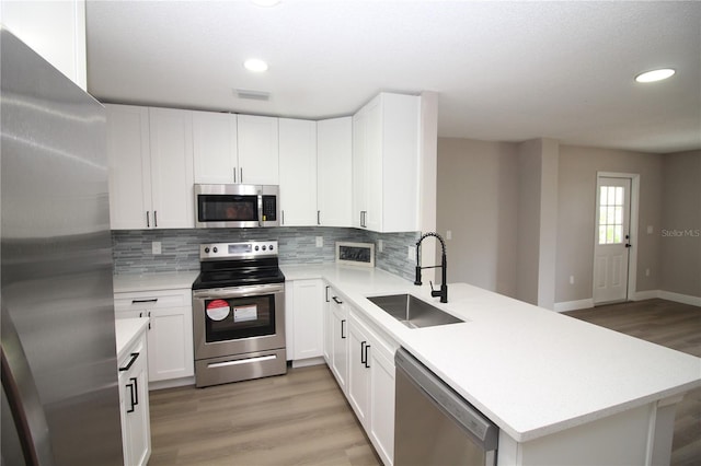 kitchen with appliances with stainless steel finishes, tasteful backsplash, sink, and light hardwood / wood-style flooring