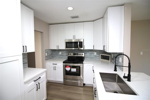 kitchen featuring dark hardwood / wood-style floors, light stone counters, white cabinets, appliances with stainless steel finishes, and backsplash