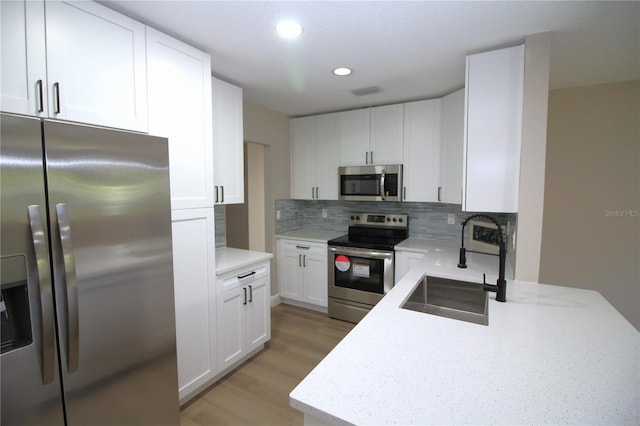 kitchen featuring appliances with stainless steel finishes, white cabinetry, backsplash, and light hardwood / wood-style flooring