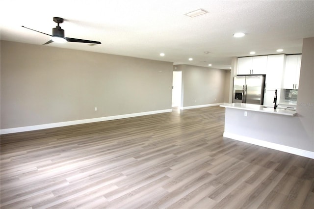 unfurnished living room featuring a textured ceiling, sink, ceiling fan, and light wood-type flooring