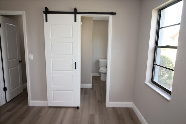 unfurnished bedroom with a barn door, connected bathroom, and dark hardwood / wood-style flooring