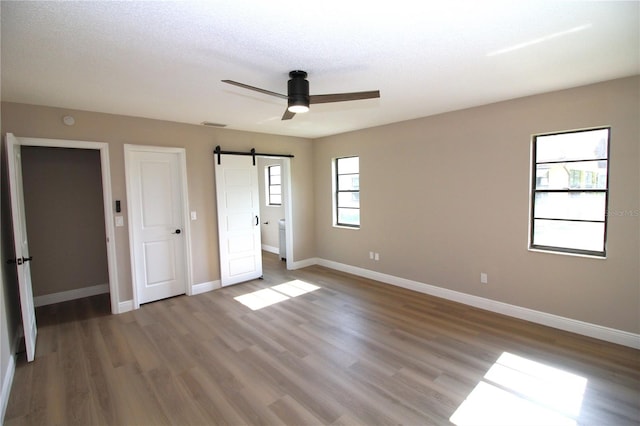 unfurnished bedroom with a barn door, a textured ceiling, wood-type flooring, and ceiling fan