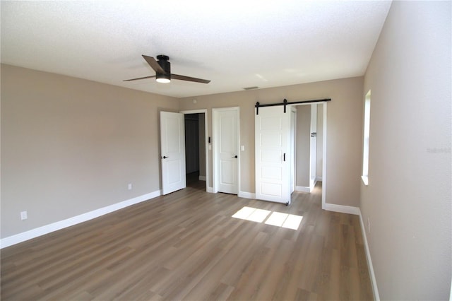 unfurnished bedroom with a barn door, ceiling fan, and dark hardwood / wood-style floors