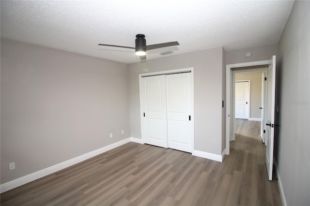 unfurnished bedroom featuring a textured ceiling, dark hardwood / wood-style flooring, a closet, and ceiling fan