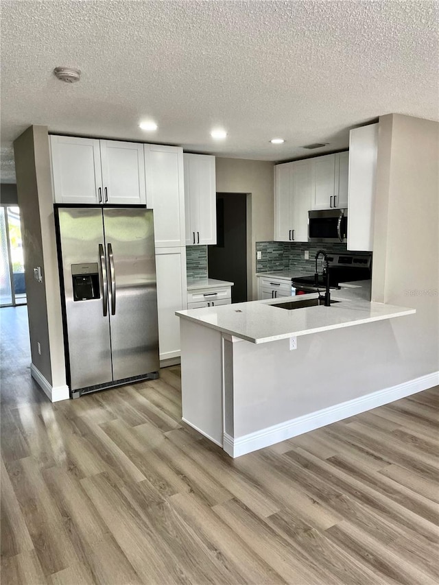 kitchen with white cabinets, appliances with stainless steel finishes, backsplash, and light hardwood / wood-style floors