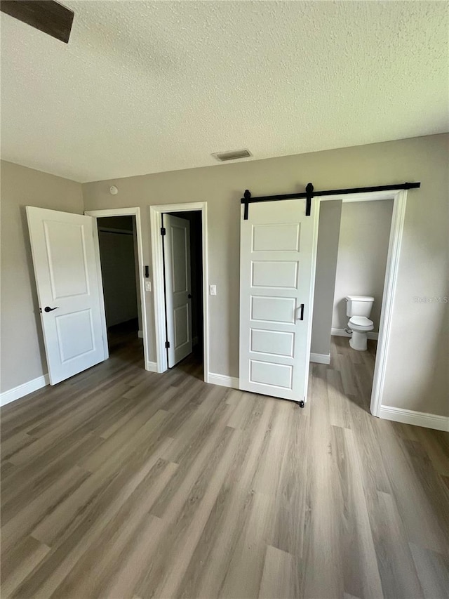 unfurnished bedroom with connected bathroom, a barn door, a textured ceiling, a closet, and light wood-type flooring