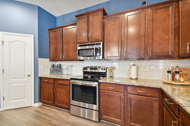 kitchen featuring light stone countertops, backsplash, light hardwood / wood-style floors, and stainless steel appliances