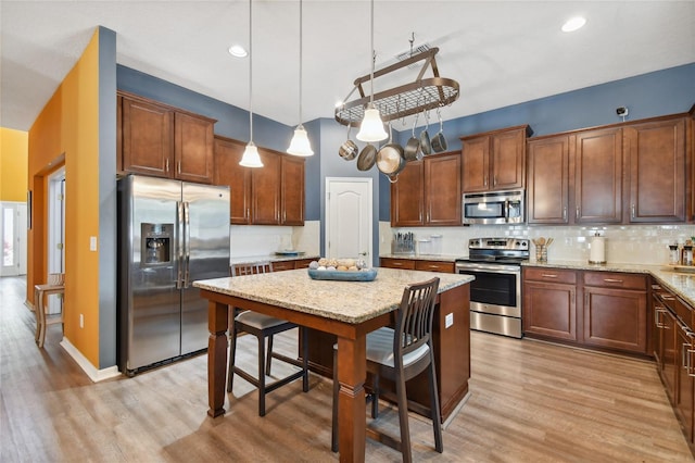 kitchen featuring light stone counters, appliances with stainless steel finishes, backsplash, light hardwood / wood-style floors, and decorative light fixtures