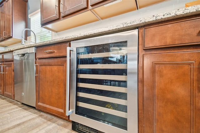 kitchen featuring stainless steel dishwasher, light stone counters, wine cooler, and light wood-type flooring