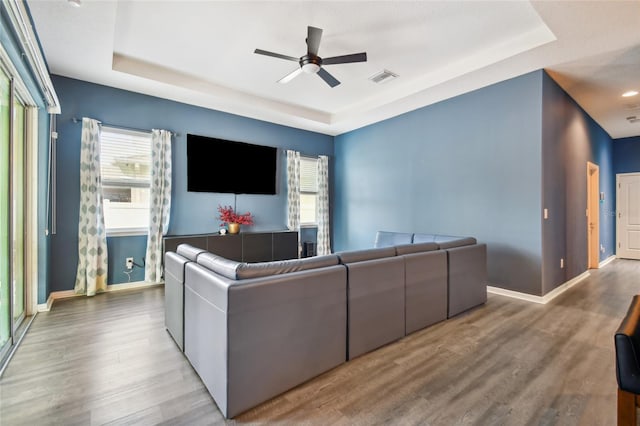 living room featuring ceiling fan, a tray ceiling, and light hardwood / wood-style flooring