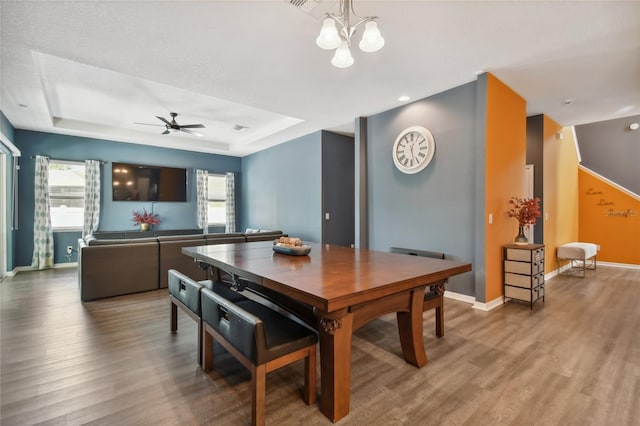 dining area with a raised ceiling, wood-type flooring, and ceiling fan with notable chandelier