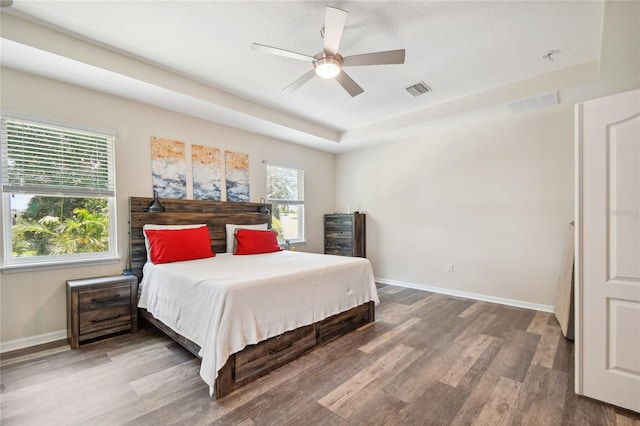 bedroom with dark hardwood / wood-style flooring, ceiling fan, and a tray ceiling