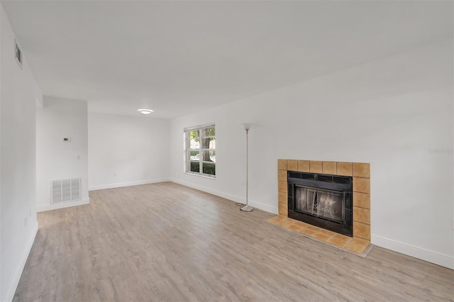 unfurnished living room featuring a tiled fireplace and light wood-type flooring