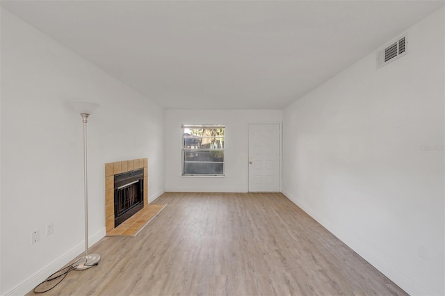 unfurnished living room featuring a tile fireplace and light hardwood / wood-style flooring