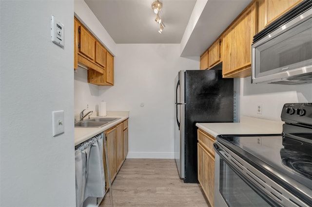 kitchen with rail lighting, stainless steel appliances, sink, and light wood-type flooring