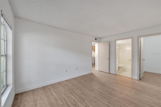 unfurnished bedroom featuring connected bathroom, a textured ceiling, and light hardwood / wood-style floors