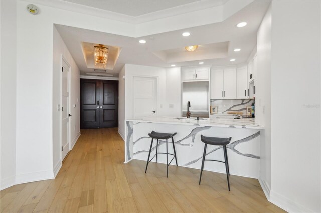 kitchen featuring white cabinetry, decorative backsplash, a tray ceiling, a breakfast bar area, and light hardwood / wood-style floors