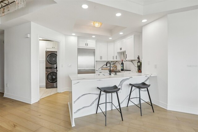 kitchen featuring stainless steel built in refrigerator, light hardwood / wood-style flooring, kitchen peninsula, stacked washer / dryer, and white cabinets