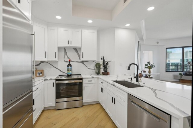 kitchen with appliances with stainless steel finishes, white cabinetry, kitchen peninsula, and sink