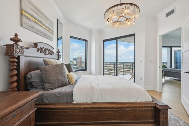 bedroom with multiple windows, an inviting chandelier, light hardwood / wood-style floors, and access to exterior