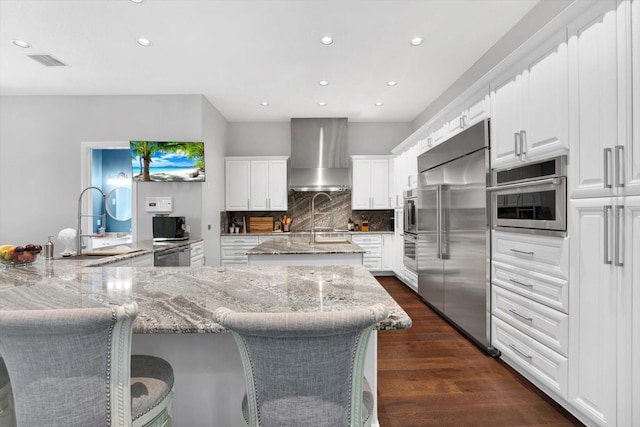 kitchen with white cabinetry, light stone counters, wall chimney exhaust hood, and appliances with stainless steel finishes